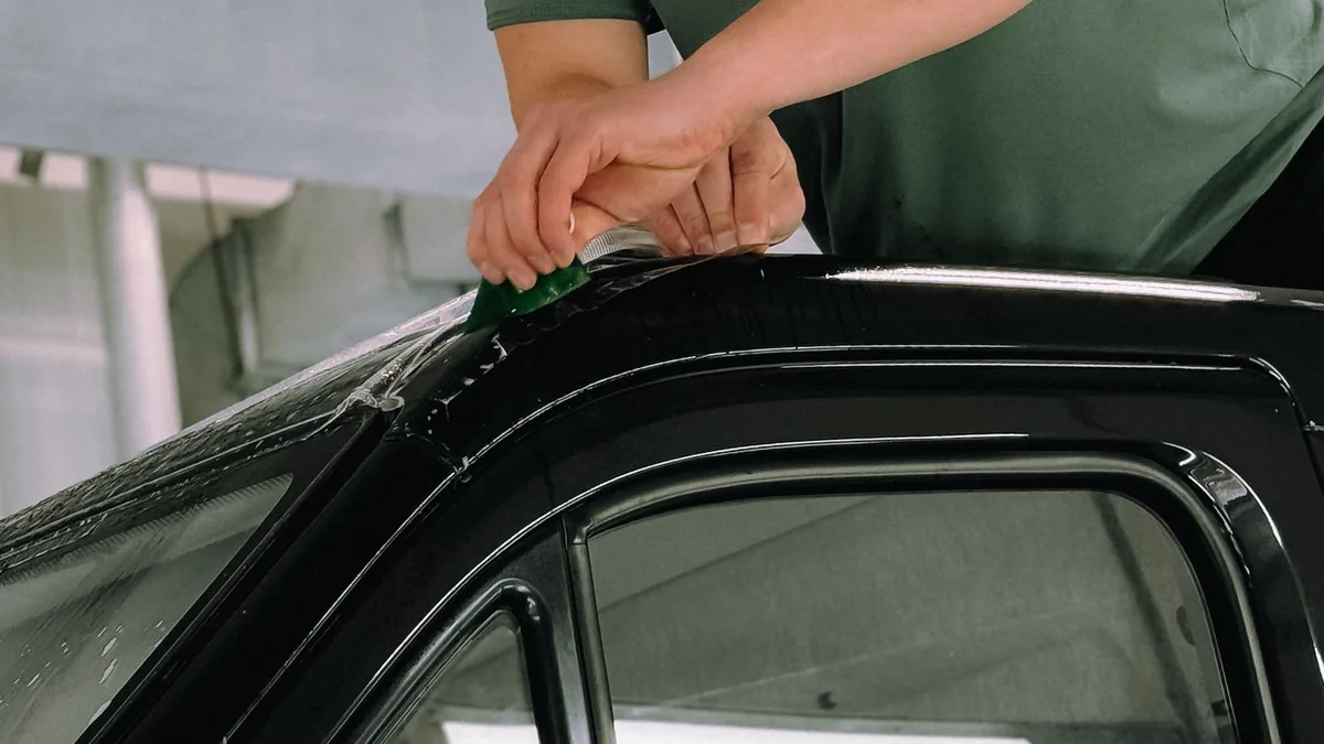 Technician fitting window film to a car's door glass