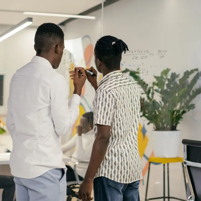 Two colleagues writing on a wall-mounted glass board