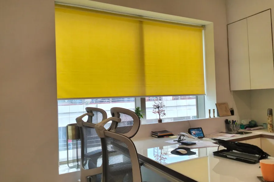 Yellow roller blind lowered over an office workstation window