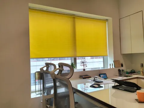 Yellow roller blind lowered over an office workstation window